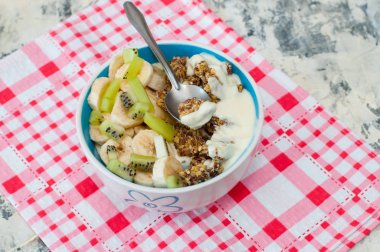 Granola Yunan yoğurt kivi ve muz pembe bir peçete üzerinde kase ile, üstten görünümü. Kaşıkta bir parça tatlı. Kilo kaybı, uygun ve lezzetli gıda için Fitness diyet