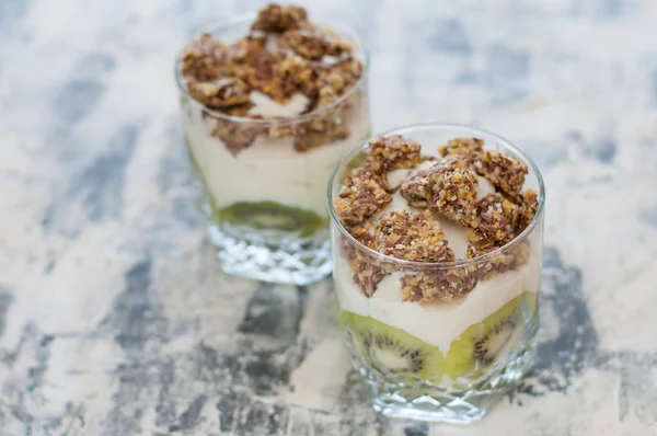 Granola, kiwi, banane et yaourt grec dans deux tasses en verre sur béton gris, espace de copie. Fitness, silhouette, corps et alimentation saine — Photo