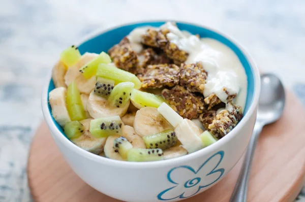 Greek yogurt and granola kiwi, banana in bowl with a spoon on a gray concrete background, view from the top. Fitness diet for weight loss, proper nutrition and a healthy lifestyle