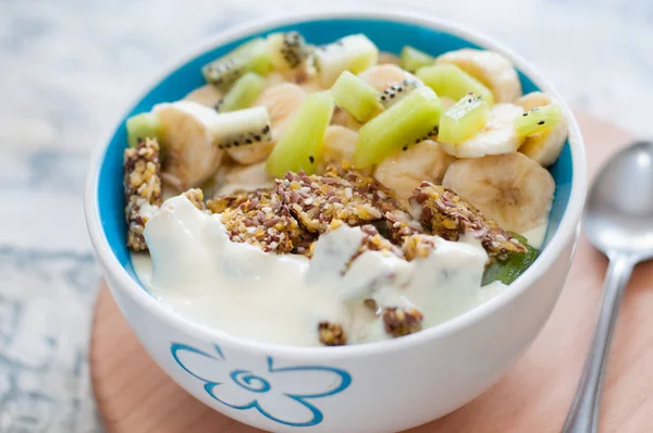 Greek yogurt, granola, kiwi and banana in bowl with a spoon on a gray concrete background, wooden tray, copy space. Fitness diet for weight loss, proper and tasty food — Stock Photo, Image
