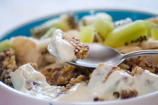 Piece of dessert on spoon close-up. Granola with Greek yogurt, kiwi and banana in a bowl. View from the side. Fitness diet for weight loss, proper and tasty food — Stock Photo, Image