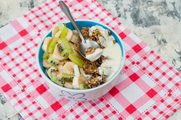 Granola con kiwi de yogur griego y plátano en un tazón en una servilleta rosa, vista desde la parte superior. Un trozo de postre en una cuchara. Dieta fitness para adelgazar, comida adecuada y sabrosa —  Fotos de Stock