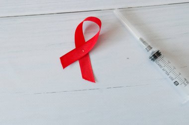 Şırınga ve kırmızı kurdele ışık ahşap arka plan üzerinde. Dünya Aids Günü.