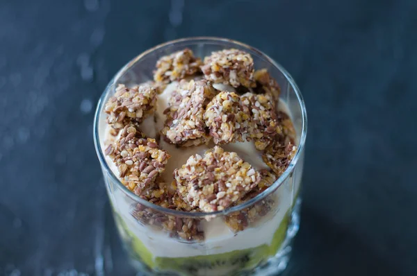 Greek yogurt, granola, banana and kiwi. Dessert in glass beaker on a dark background, close-up macro. Concept body and healthy food — Stock Photo, Image