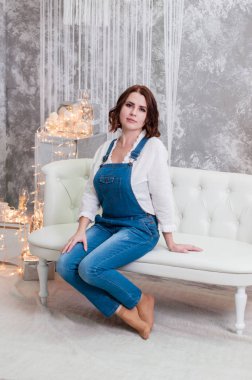 Çok güzel gülümseyen kadın bir çelenk ve Noel süslemeleri yakınında beyaz bir kanepede oturan.