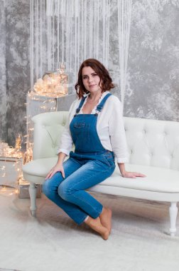 Çok güzel gülümseyen kahverengi saçlı kadın çelenk ve yeni yıl süslemeleri yakın beyaz bir kanepede oturan