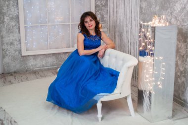 Yeni yıl çelenk yakınındaki bir kanepede oturan mavi bir gece elbisesi kıvırcık saçlı çok güzel kahverengi saçlı kadın