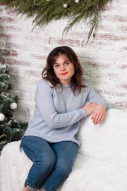 Yeni yıl ağacının yanında beyaz bir kanepede oturan kıvırcık saçlı pensive güzel kahverengi saçlı kadın