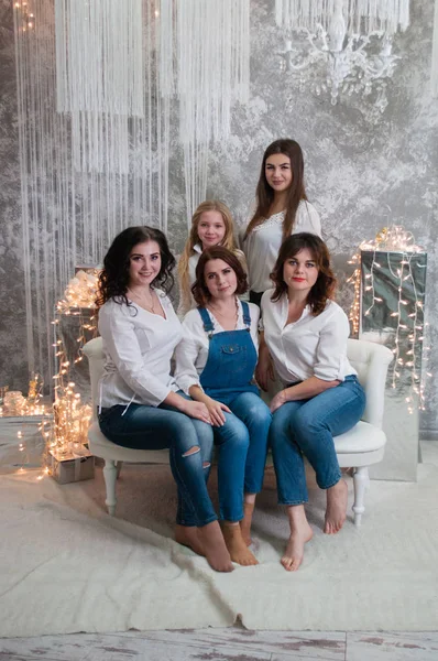 A companhia de meninas bonitas celebra o Natal, o Ano Novo. Meninas no interior do Ano Novo da sala estão sentados em um sofá branco contra o fundo de guirlandas — Fotografia de Stock