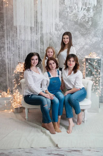 A companhia de meninas bonitas celebra o Natal, o Ano Novo. Meninas no interior do Ano Novo da sala estão sentados em um sofá branco contra o fundo de guirlandas — Fotografia de Stock