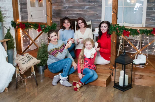 Várias mulheres muito bonitas e uma adolescente celebram o Natal, o ano novo. Meninas no interior do Ano Novo com copos em suas mãos estão sentados nos degraus — Fotografia de Stock