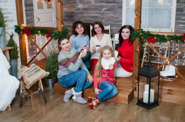 Birkaç çok güzel kadın ve bir genç kız Noel kutlamak, yeni yıl. Ellerinde bardaklarla yeni yıl iç mekandaki kızlar merdivenlerde oturuyorlar.