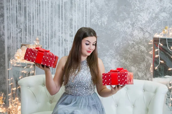 Nagyon szép és szexi nő egy szürke estélyi ruha két ajándékot a kezükben. A lány nézi az ajándékokat, és úgy gondolja, hogy mi dobozt nyitni. — Stock Fotó