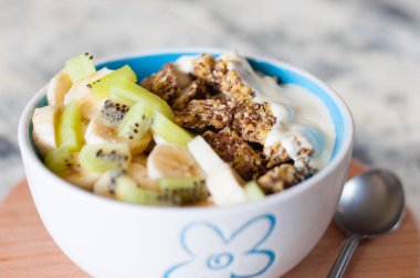 Yunan yoğurt, granola, kivi ve muz gri beton arka plan, ahşap tepsi, yakın çekim bir kase içinde. Kilo kaybı, uygun ve lezzetli gıda için Fitness diyet