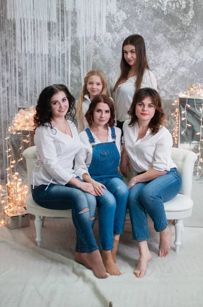 A companhia de meninas bonitas celebra o Natal, o Ano Novo. Meninas no interior do Ano Novo da sala estão sentados em um sofá branco contra o fundo de guirlandas — Fotografia de Stock