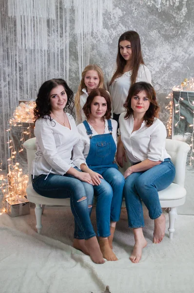 La compagnia di belle ragazze festeggia il Natale, il nuovo anno. Le ragazze all'interno della stanza del nuovo anno sono sedute su un divano bianco sullo sfondo delle ghirlande — Foto Stock