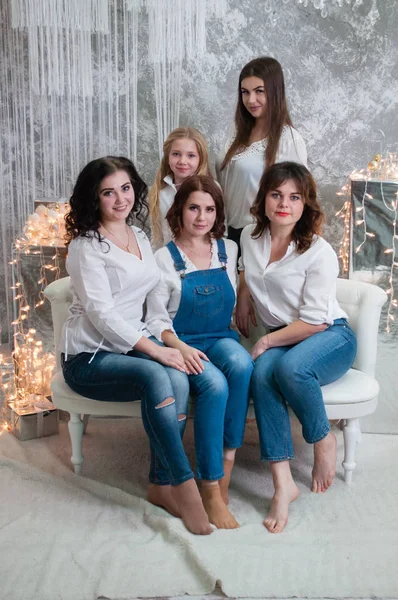 La compagnia di belle ragazze festeggia il Natale, il nuovo anno. Le ragazze all'interno della stanza del nuovo anno sono sedute su un divano bianco sullo sfondo delle ghirlande — Foto Stock