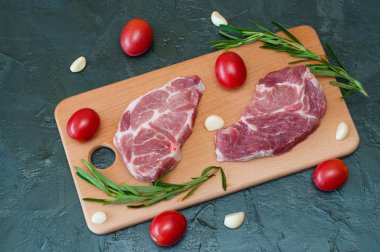 Domatesli çiğ domuz bifteği, sarımsak ve ahşap bir tahtada biberiye.