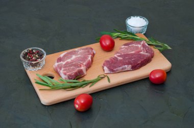 Çiğ et biftekleri, kırmızı domatesler, biberiye, deniz tuzu, koyu arkaplanda biber.