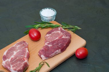 Çiğ et biftekleri, kırmızı domatesler, biberiye ve tuz koyu arka planda ve sağa metin eklemek için bir yer