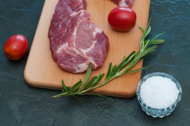 Çiğ domuz eti, biberiye, domates ve tuz ahşap kesim tahtasında, koyu arka plan, üst görüş ve yan görüş.