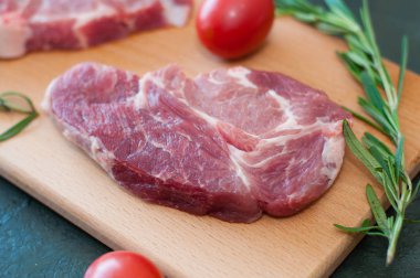 Çiğ domuz eti, biberiye ve domates parçaları kesim tahtasında, koyu gri beton arka planda, yakın plan