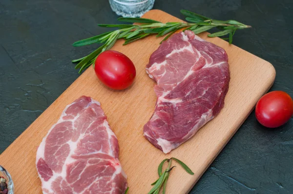 Çiğ et, domates, biberiye, siyah arka planda tuz ve biber.