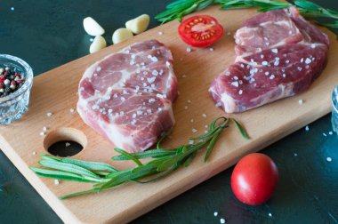 Kesme tahtasındaki çiğ et, tuz ve biber serpilmiş, sarımsak, biberiye ve domates, üst görüş ve yan görüş.