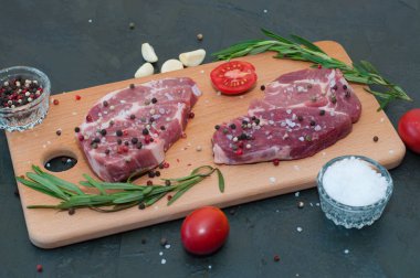 Kesme tahtasındaki çiğ et, tuz ve biber serpilmiş, sarımsak, biberiye ve domates, üst görüş ve yan görüş.