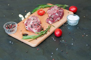 Kesme tahtasında çiğ et, tuz ve biber serpiştirilmiş, sarımsak, biberiye ve domates, üst görüş ve yan görüş.