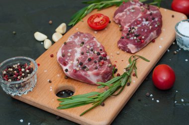 Kesme tahtasında çiğ et, tuz ve biber serpiştirilmiş, sarımsak, biberiye ve domates, üst ve yan görünüm.