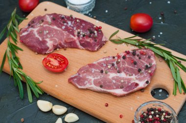 Kesme tahtasında çiğ et, tuz ve biber serpiştirilmiş, sarımsak, biberiye ve domates, üst ve yan görünüm.