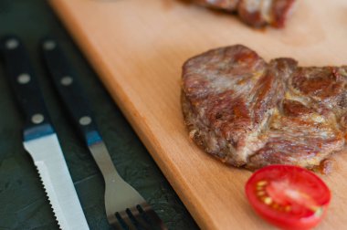 Izgara dana eti, biftek ya da domuz eti, domates, biberiye ve soya sosu et, bıçak ve çatal için, ahşap bir tahtanın üzerinde, yakın plan.