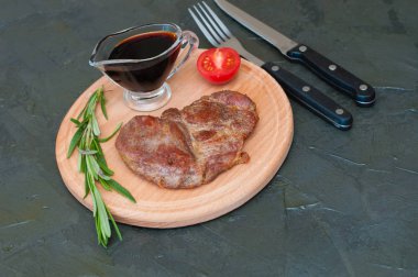 Kızarmış, lezzetli dana eti, biftek ya da domuz eti, domates, biberiye ve soya sosu yuvarlak ahşap tahtada, bıçakta ve çatalda et için.,