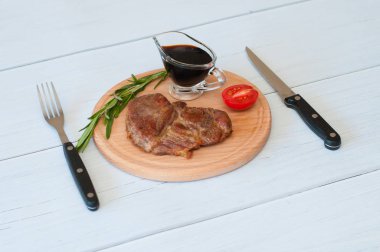 Kızarmış, lezzetli dana eti, biftek ya da domuz eti, domates, biberiye ve soya sosu yuvarlak ahşap tahtada, hafif arka planda, bıçak ve çatal üzerinde.