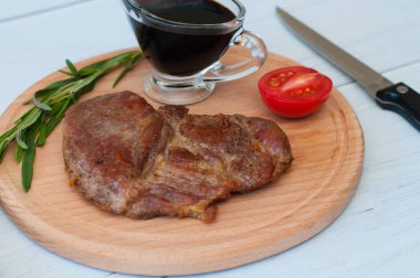 Kızarmış, lezzetli dana eti, biftek ya da domuz eti, domates, biberiye ve soya sosu yuvarlak ahşap bir tahtada, hafif bir arka planda, bıçak ve çatal, yakın plan