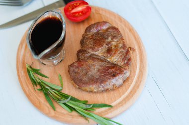 Pişmiş, ahşap bir tahtanın üzerinde ızgara domuz eti, soya sosu, biberiye ve domates, açık arkaplanda.