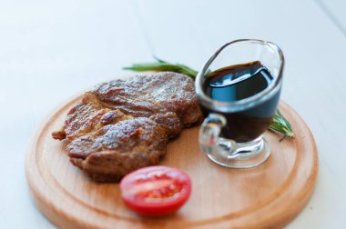 Ahşap bir tahtanın üzerinde pişmiş, ızgara domuz bifteği, soya sosu, biberiye ve domates ile birlikte fotokopi alanı ile hafif arka planda.