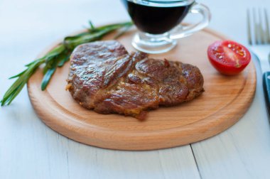 Ahşap bir tahtanın üzerinde pişmiş, ızgara domuz bifteği, soya sosu, biberiye ve domates ile birlikte fotokopi alanı ile hafif arka planda.