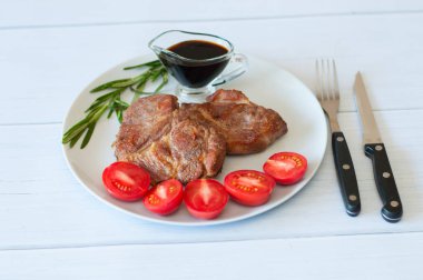 Sos, biberiye ve domatesli gri bir tabakta hafif ahşap arka planda leziz domuz bifteği.