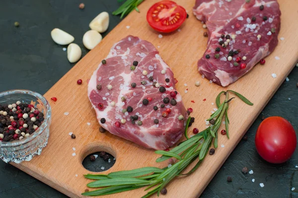 Kesme tahtasındaki çiğ et, tuz ve biber serpilmiş, sarımsak, biberiye ve domates, üst görüş ve yan görüş.