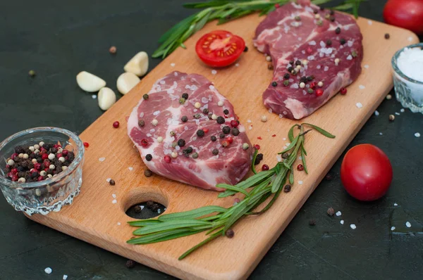 Kesme tahtasında çiğ et, tuz ve biber serpiştirilmiş, sarımsak, biberiye ve domates, üst ve yan görünüm.