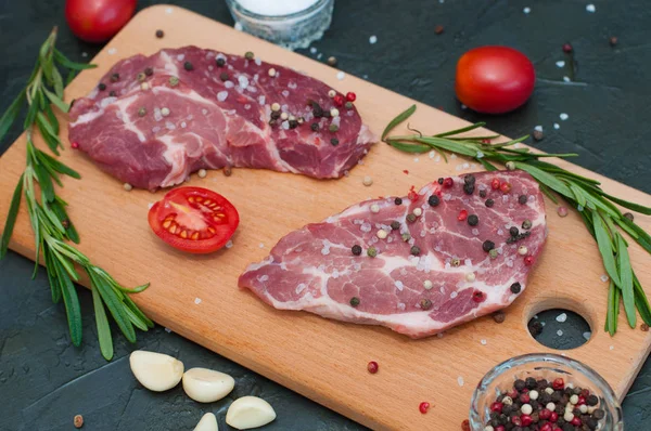 Kesme tahtasında çiğ et, tuz ve biber serpiştirilmiş, sarımsak, biberiye ve domates, üst ve yan görünüm.