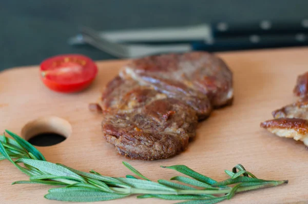 Grilované telecí, hovězí nebo vepřový steak, rajčata, rozmarýn a sójová omáčka na maso, nůž a vidličku, na dřevěné desce, zblízka — Stock fotografie