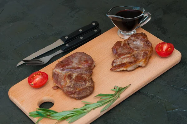 Izgara dana eti, biftek ya da domuz eti, domates, biberiye ve soya sosu et, bıçak ve çatal, ahşap bir tahtanın üzerinde, yakın plan, düz yatak