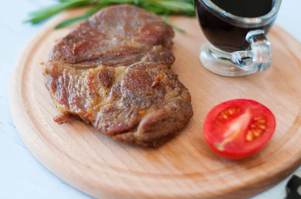 Filete de cerdo cocido a la parrilla sobre una tabla redonda de madera, con salsa de soja, romero y tomate — Foto de Stock