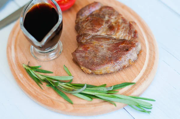 Pişmiş, ahşap bir tahtanın üzerinde ızgara domuz eti, soya sosu, biberiye ve domates, açık arkaplanda.