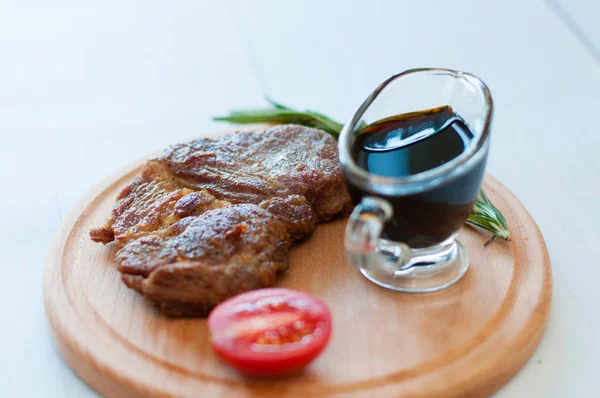 Ahşap bir tahtanın üzerinde pişmiş, ızgara domuz bifteği, soya sosu, biberiye ve domates ile birlikte fotokopi alanı ile hafif arka planda.