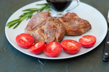 Baharatlı, domatesli ve soslu kokulu domuz eti bifteği gri bir tabakta, metin için yeri olan koyu beton arka planda.