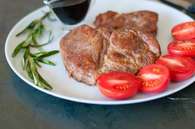 Biberiyeli, domatesli ve soslu leziz domuz eti bifteği. Gri tabakta, yakın plan.